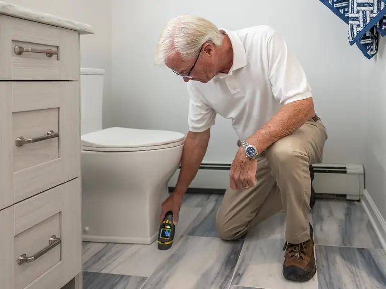 Plumber kneeling beside a toilet with a flashlight